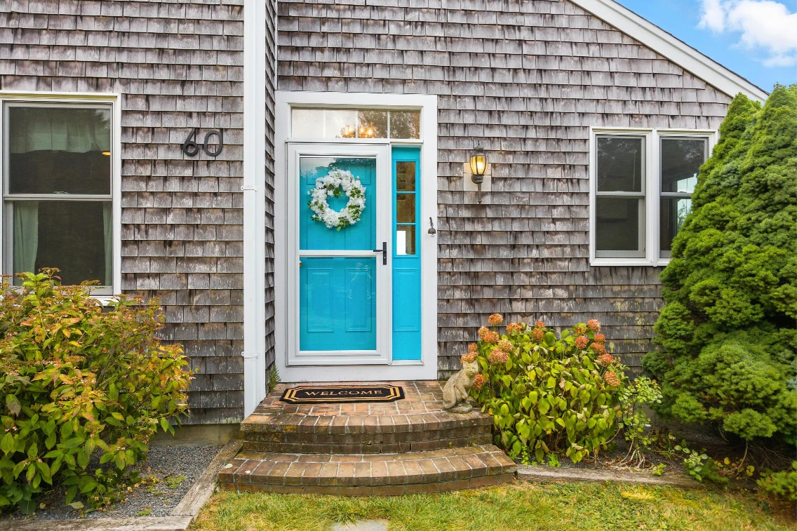 Welcoming front entrance with a turquoise door, floral wreath, and landscaped steps leading to a cozy Cape Cod retreat.