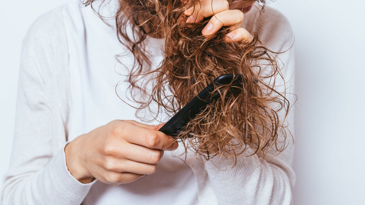 A person using a flat iron on curly hair to achieve smoother, shinier locks.