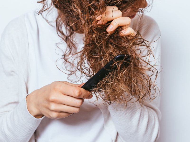 A person using a flat iron on curly hair to achieve smoother, shinier locks.