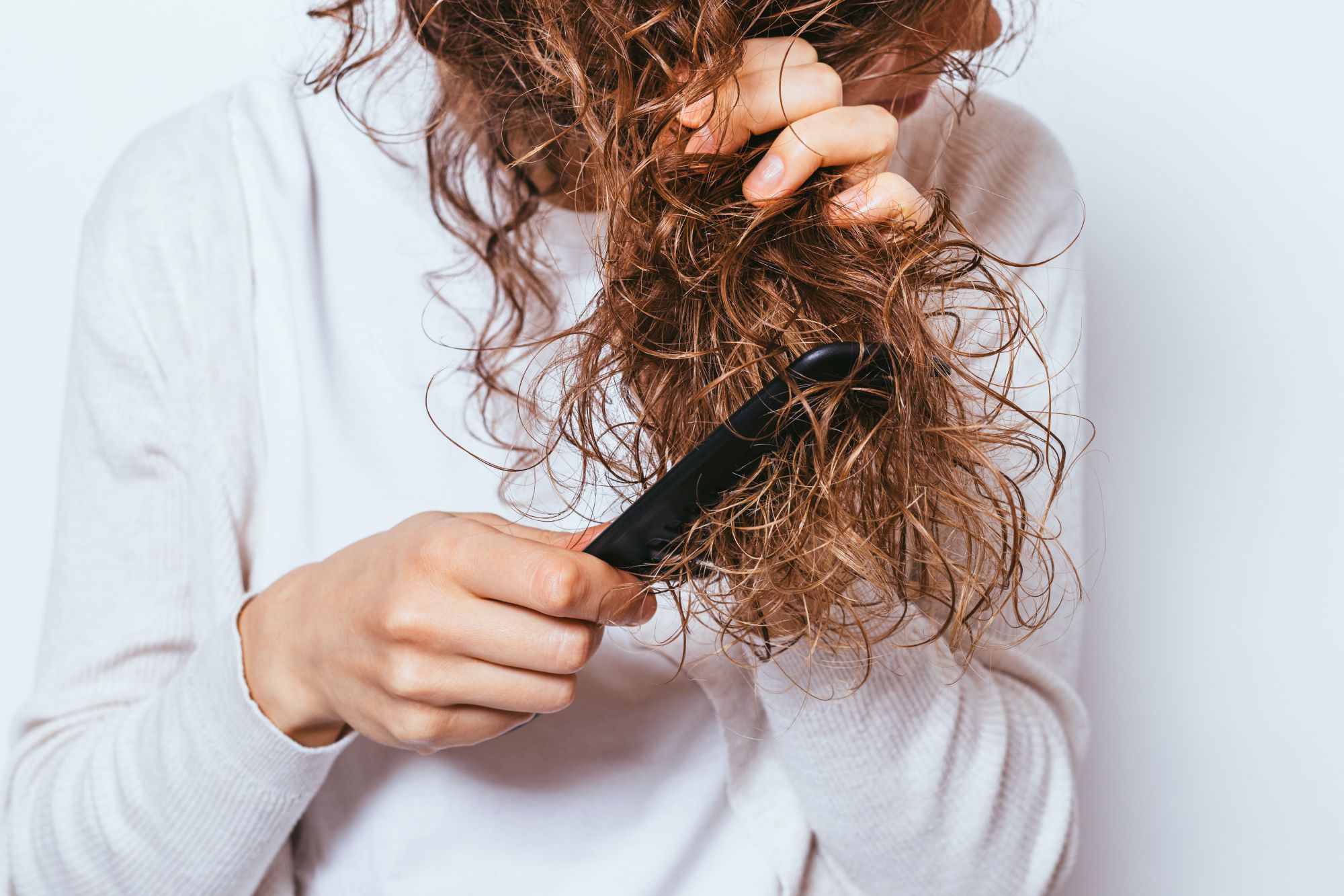 A person using a flat iron on curly hair to achieve smoother, shinier locks.