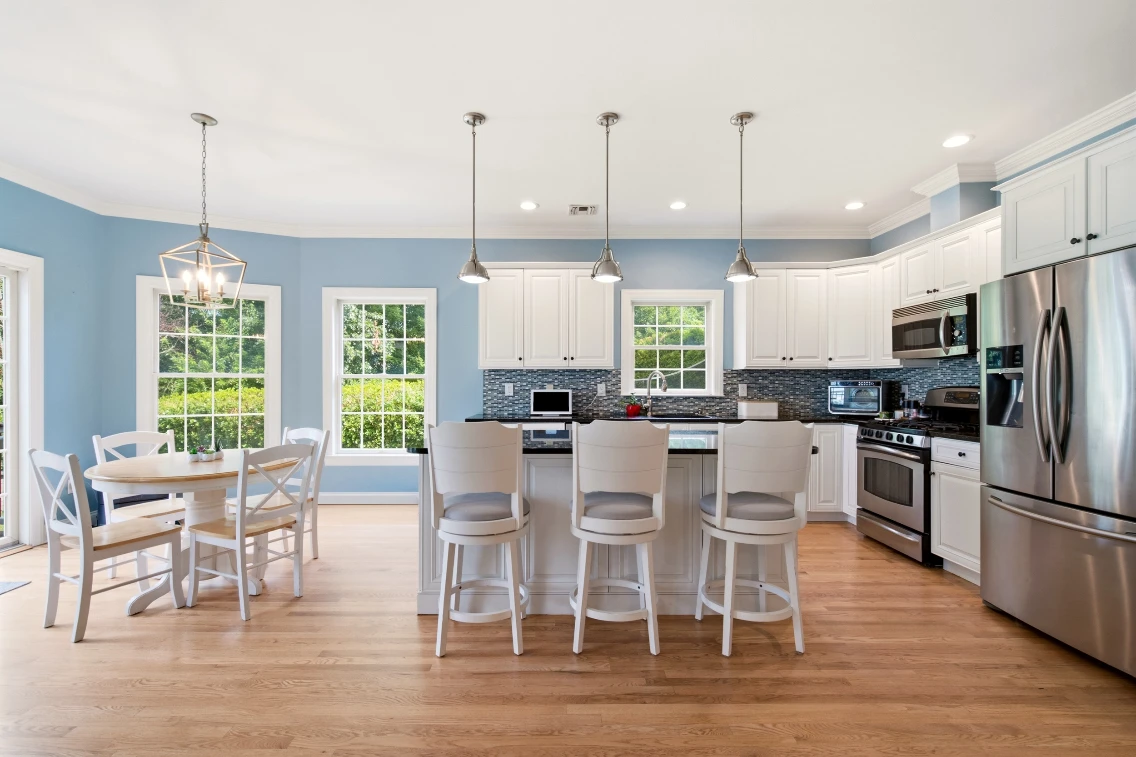 Modern kitchen with white cabinetry, gray countertops, and a dining area featuring a round table and chairs near large windows.