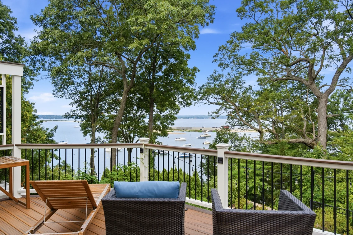 Modern patio overlooking the water in Eatons Neck, featuring lounge chairs and a scenic view of boats and greenery.