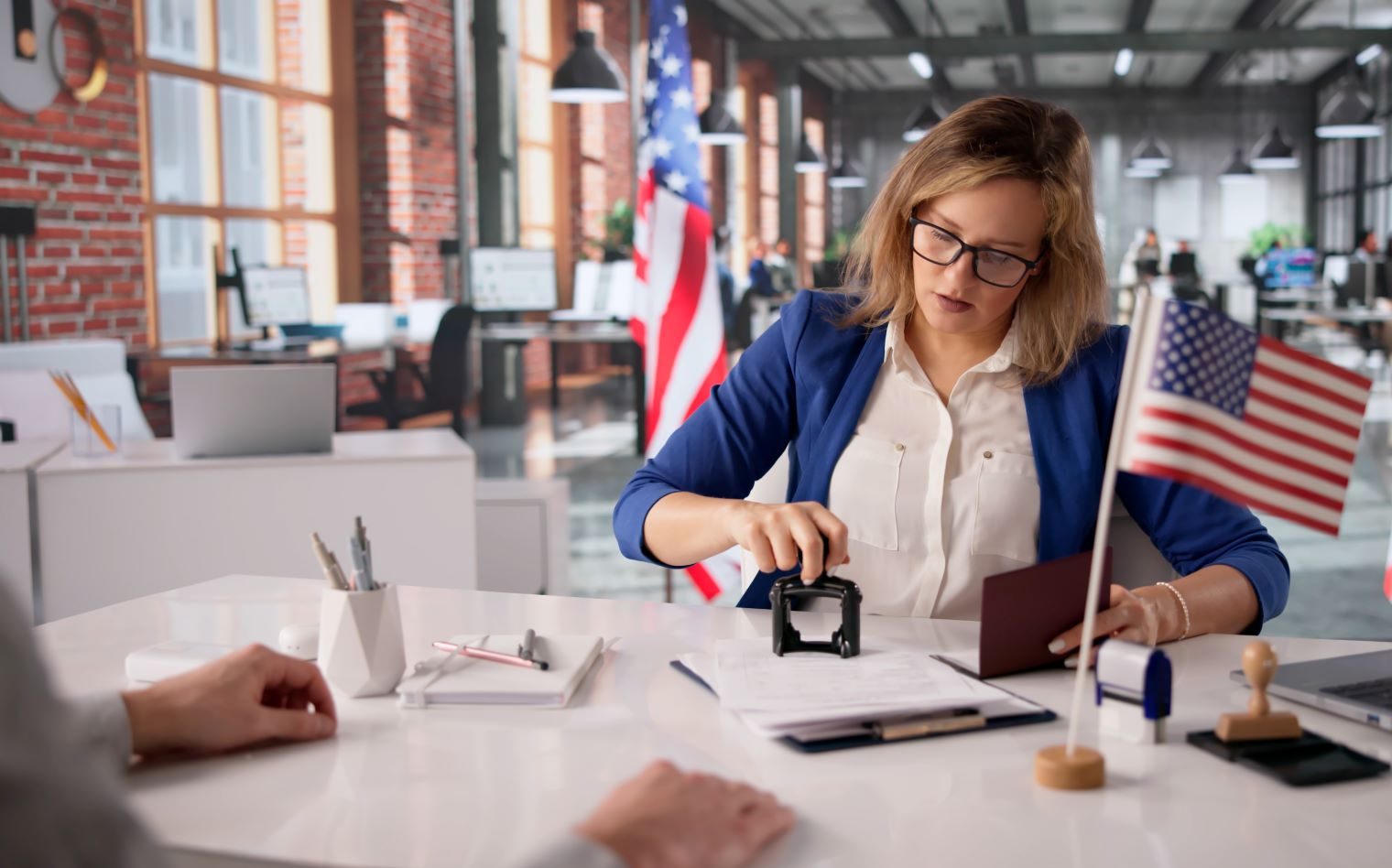 An immigration officer reviews documents and uses a stamp in an office decorated with American flags.