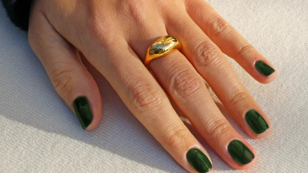 Olive green nail polish on fingers, accented with a gold ring, showcasing autumn-inspired nail fashion.