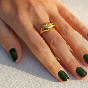Olive green nail polish on fingers, accented with a gold ring, showcasing autumn-inspired nail fashion.