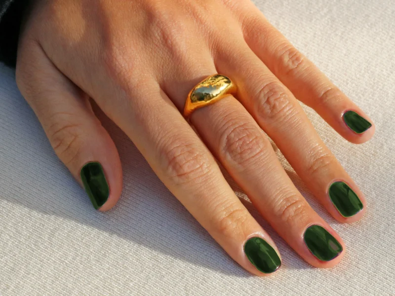Olive green nail polish on fingers, accented with a gold ring, showcasing autumn-inspired nail fashion.