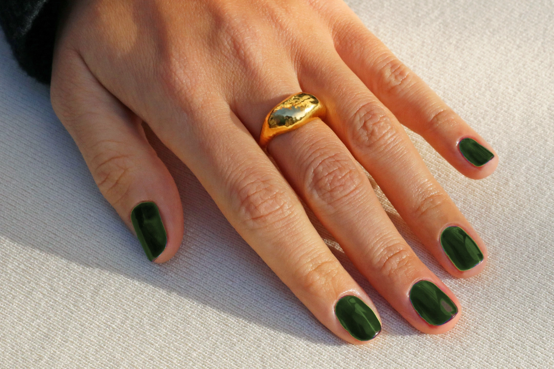 Olive green nail polish on fingers, accented with a gold ring, showcasing autumn-inspired nail fashion.