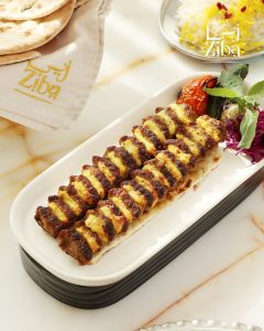 Grilled kebabs served on a platter with herbs, tomatoes, and flatbread reflecting contemporary Persian dining.