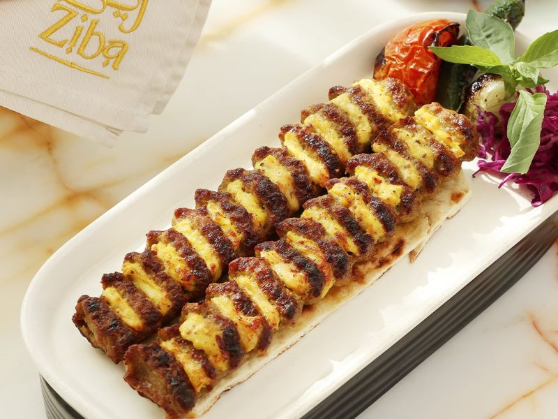 Grilled kebabs served on a platter with herbs, tomatoes, and flatbread reflecting contemporary Persian dining.