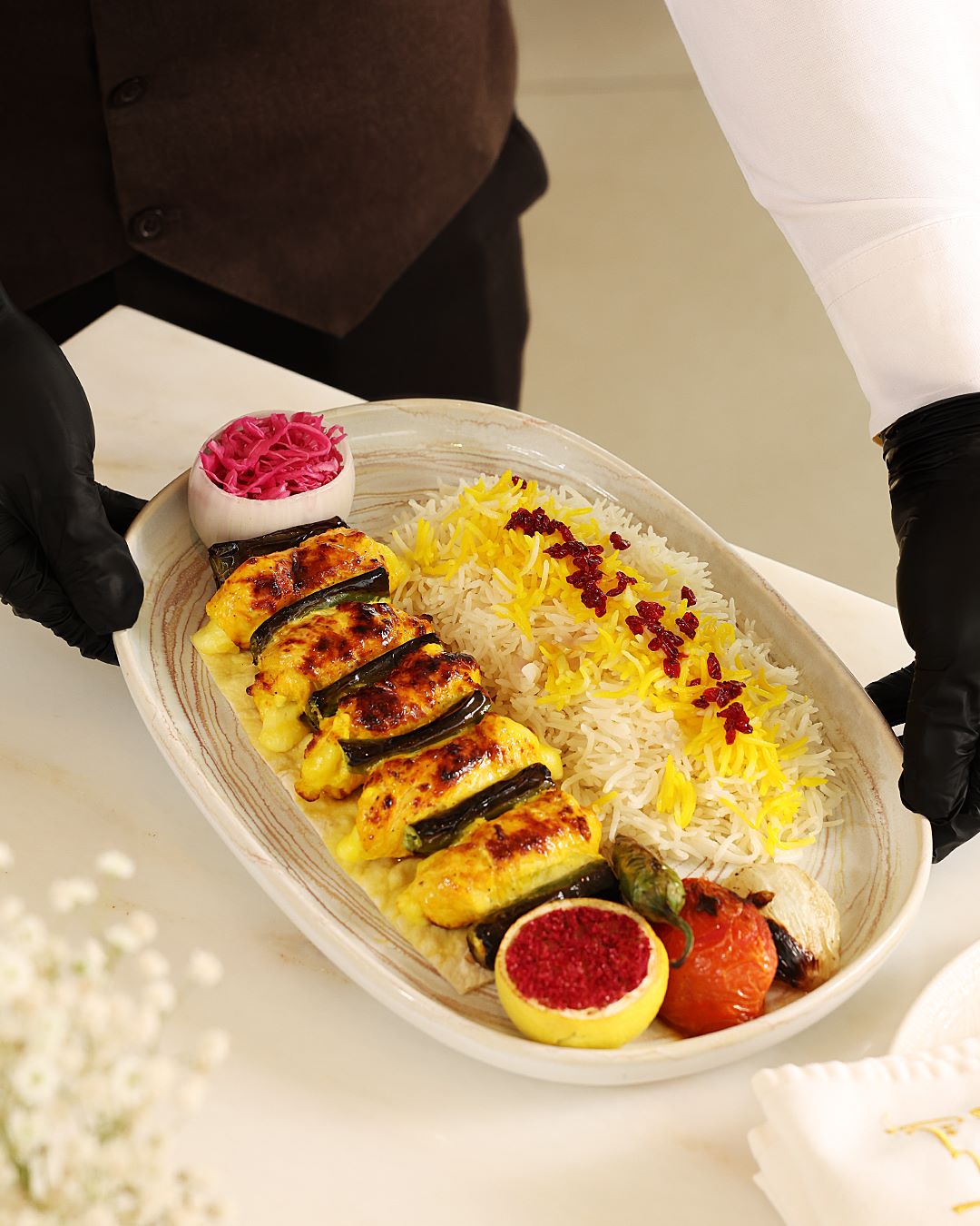 Grilled Persian kebabs served with saffron rice, lemon, pickled onions, and garnishes on a large oval plate.