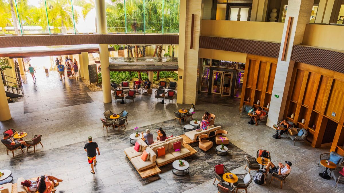 Spacious lobby with seating areas and indoor plants, showcasing guests enjoying leisure time at a luxury resort.