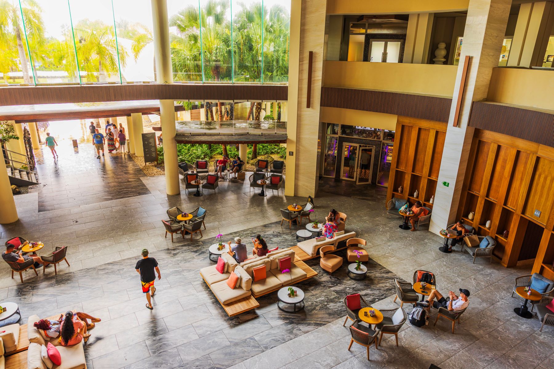 Spacious lobby with seating areas and indoor plants, showcasing guests enjoying leisure time at a luxury resort.