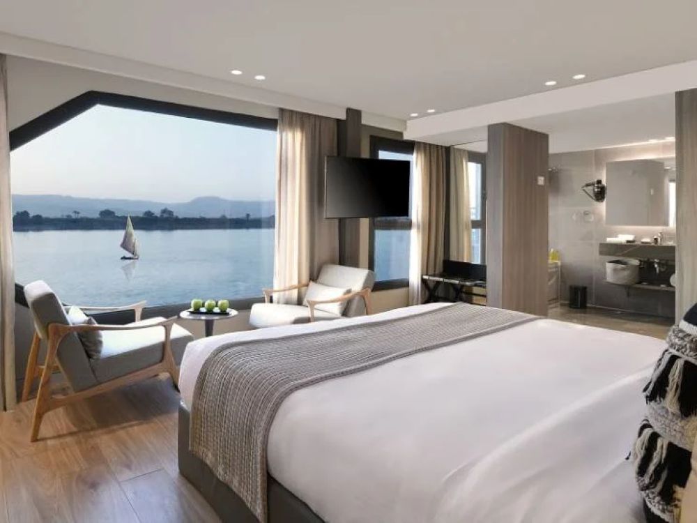 Luxurious bedroom in a Nile cruise suite featuring modern decor, large windows with river views, and stylish seating.