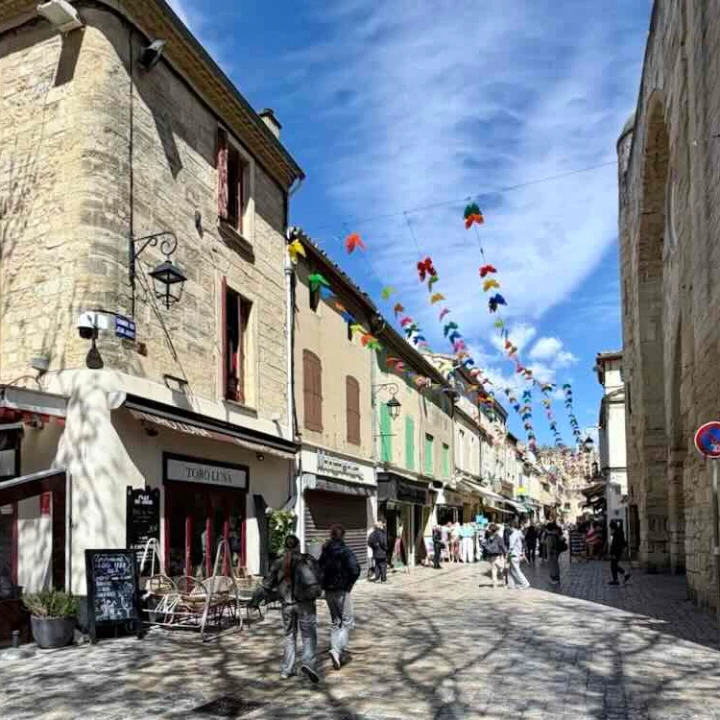 Charming street in Aigues-Mortes, featuring medieval architecture and colorful decorations hanging overhead.