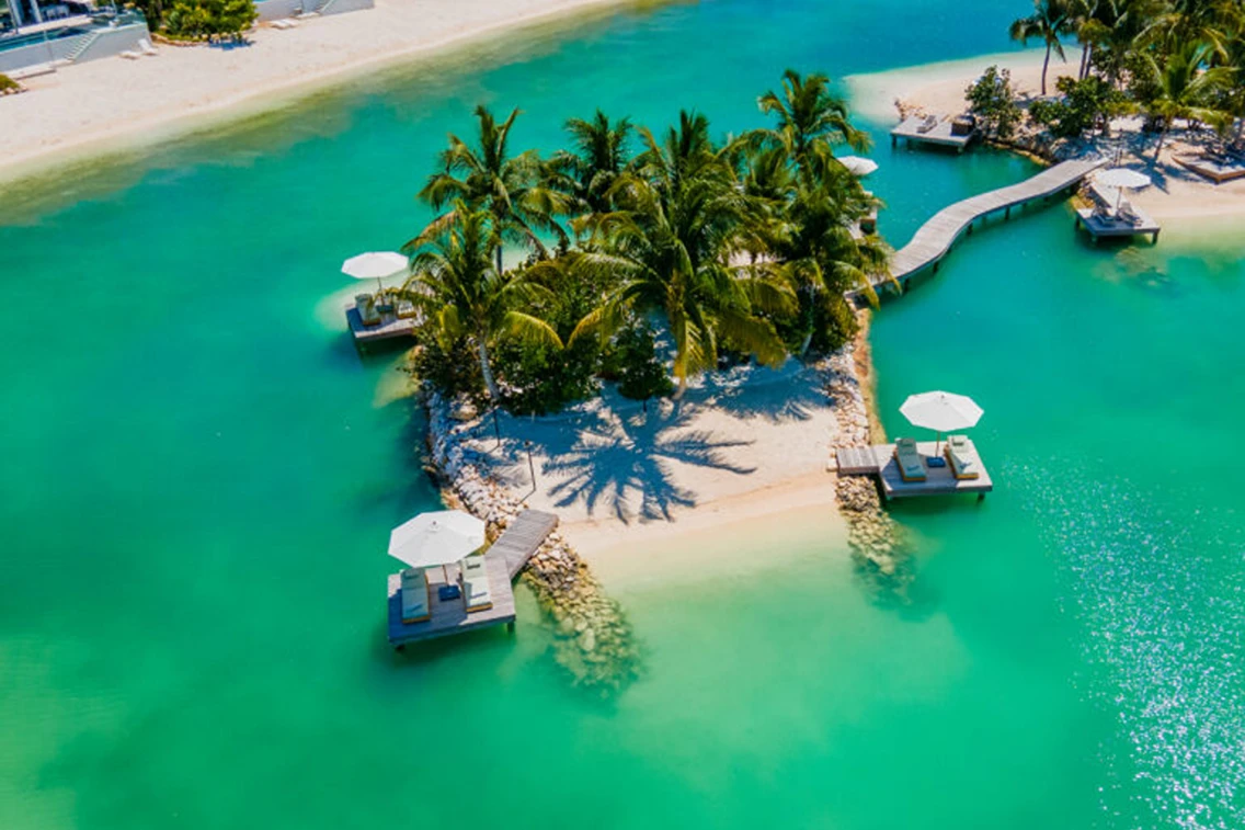 Tropical island with palm trees and lounge chairs surrounded by clear turquoise water in Turks & Caicos.