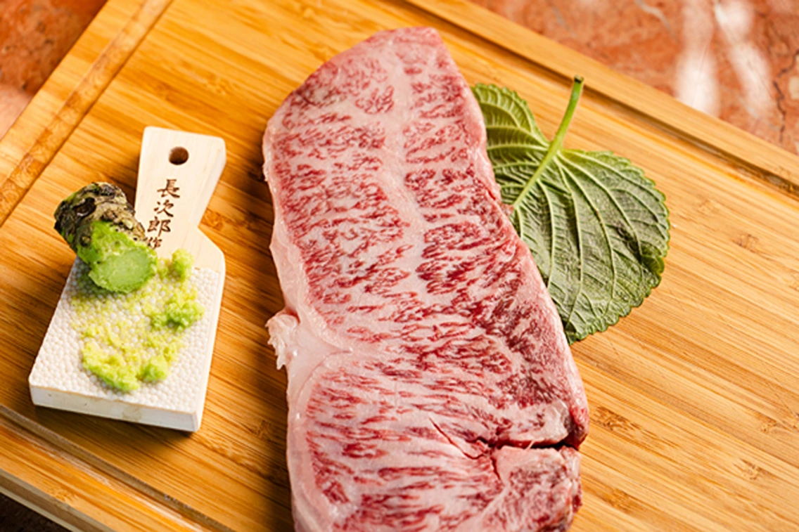 Exceptional marbled steak accompanied by freshly prepared wasabi and a shiso leaf on a wooden cutting board.