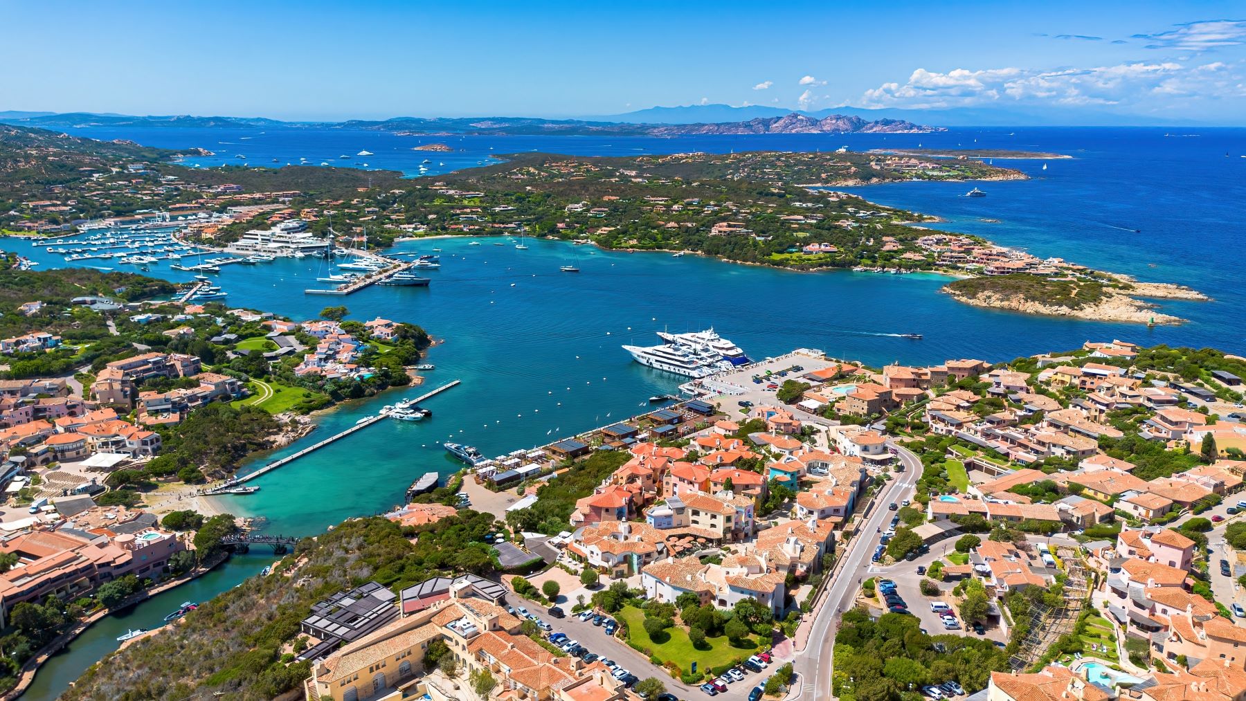 Aerial view of a coastal town in Italy featuring marinas, boats, and lush greenery along a vibrant blue sea.