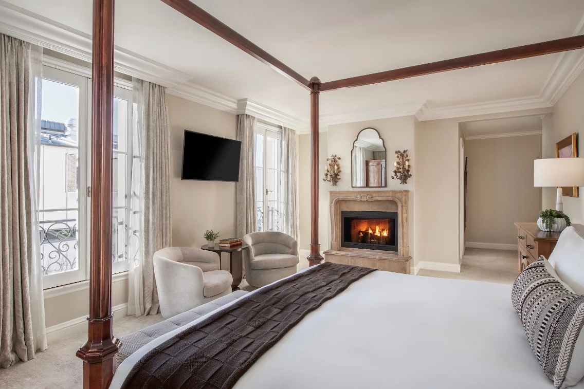 Luxurious bedroom featuring a four-poster bed, cozy seating area, modern fireplace, and large windows with natural light.