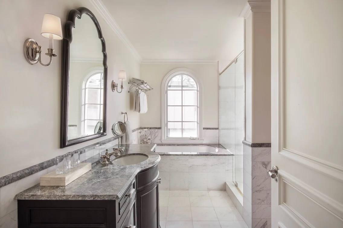 Elegant bathroom with marble finishes, a large tub, a double sink, and natural light from a window.