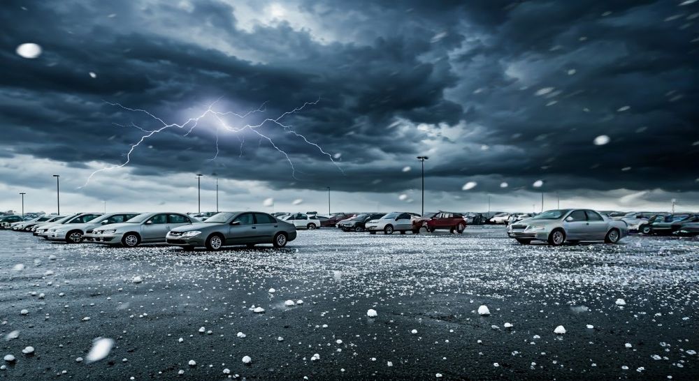 A parking lot filled with cars under a stormy sky, with lightning and hail covering the ground.