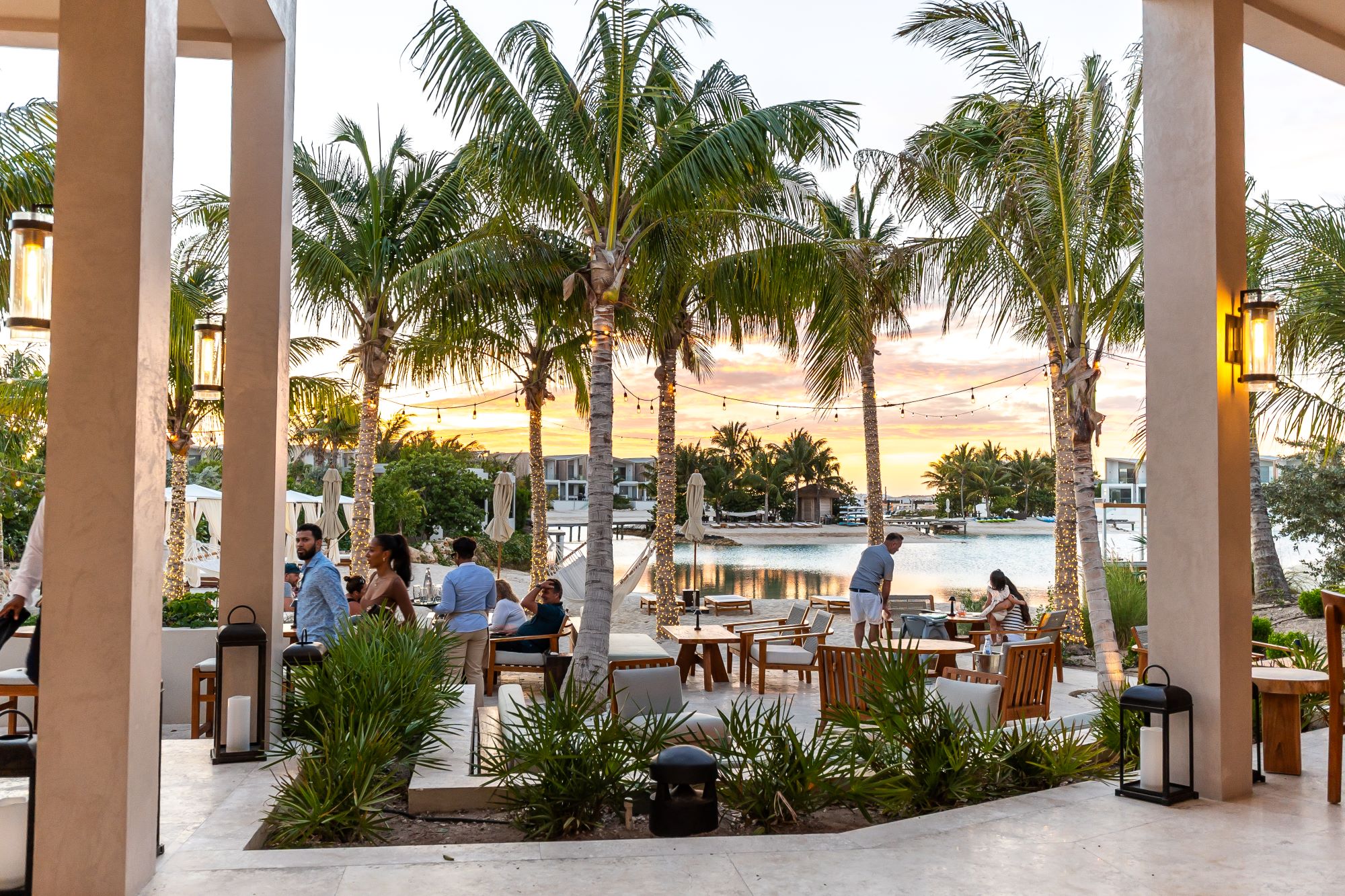 Relaxed outdoor dining area surrounded by palm trees at sunset, with guests enjoying the waterfront view in Turks & Caicos.