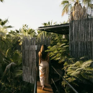 A woman walks along a wooden pathway surrounded by lush greenery at Acre Resort in Los Cabos.