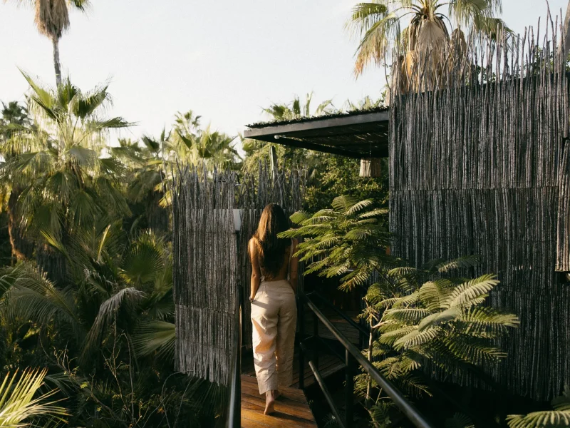 A woman walks along a wooden pathway surrounded by lush greenery at Acre Resort in Los Cabos.
