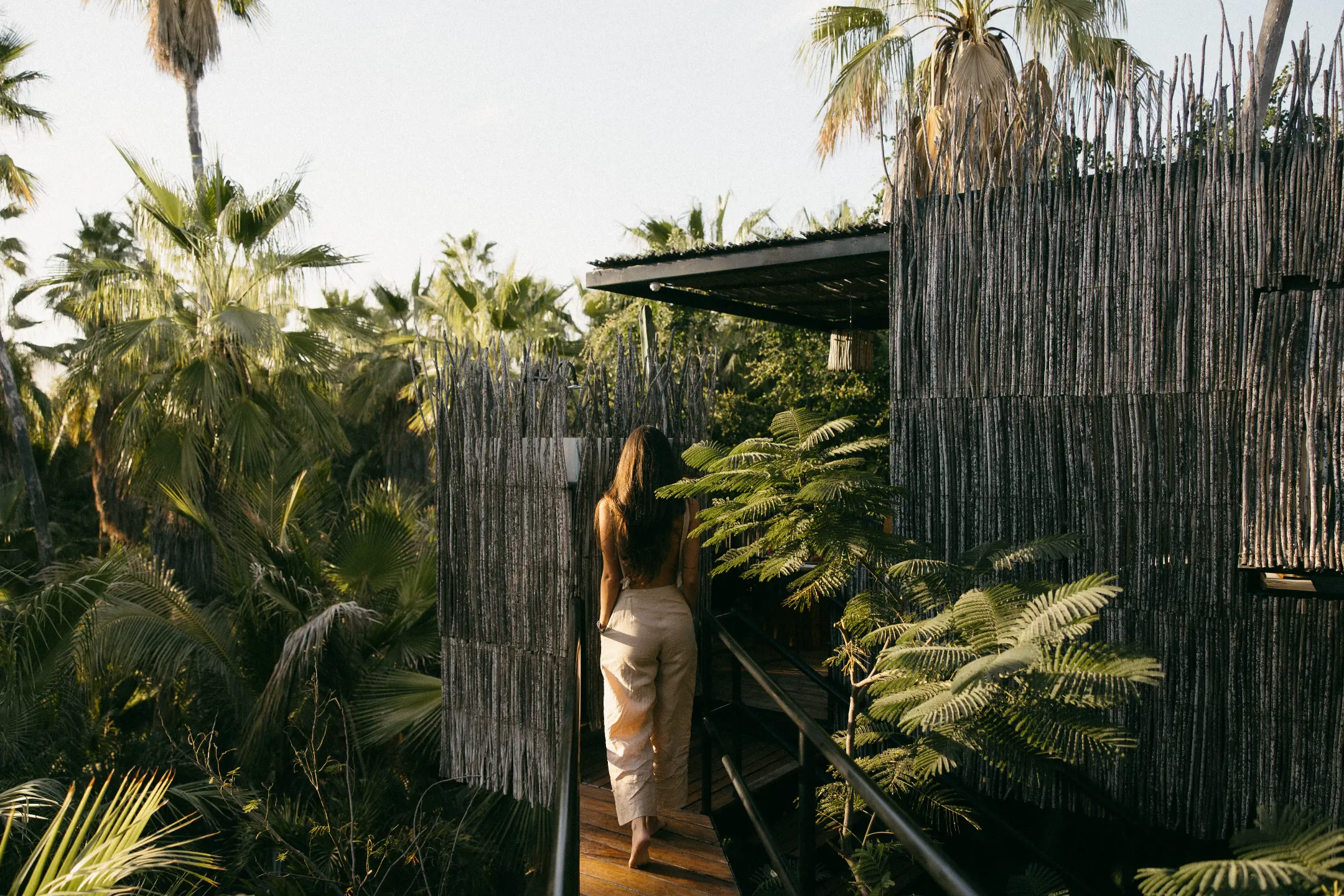 A woman walks along a wooden pathway surrounded by lush greenery at Acre Resort in Los Cabos.
