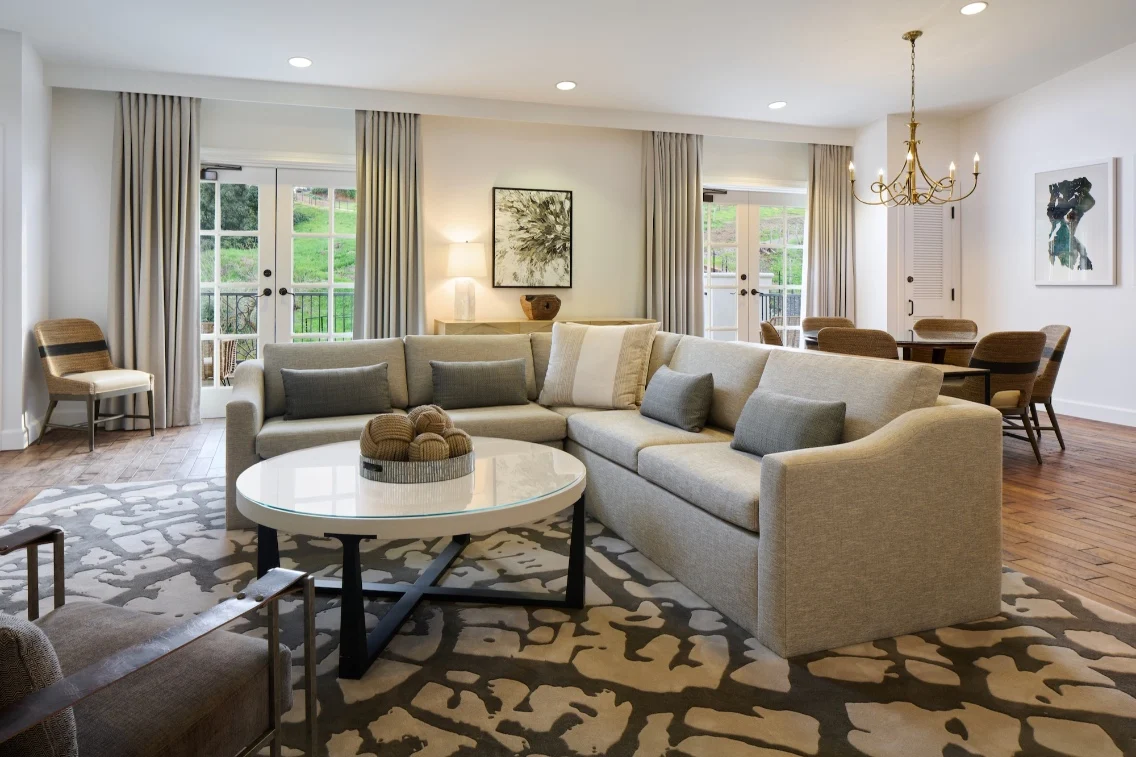 Sophisticated living room in a Napa Valley hotel suite, featuring a sectional sofa, coffee table, and dining area with natural light.