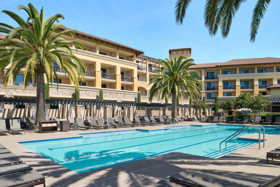 A pristine pool surrounded by palm trees and lounge chairs, with the Meritage Resort & Spa buildings in the background.