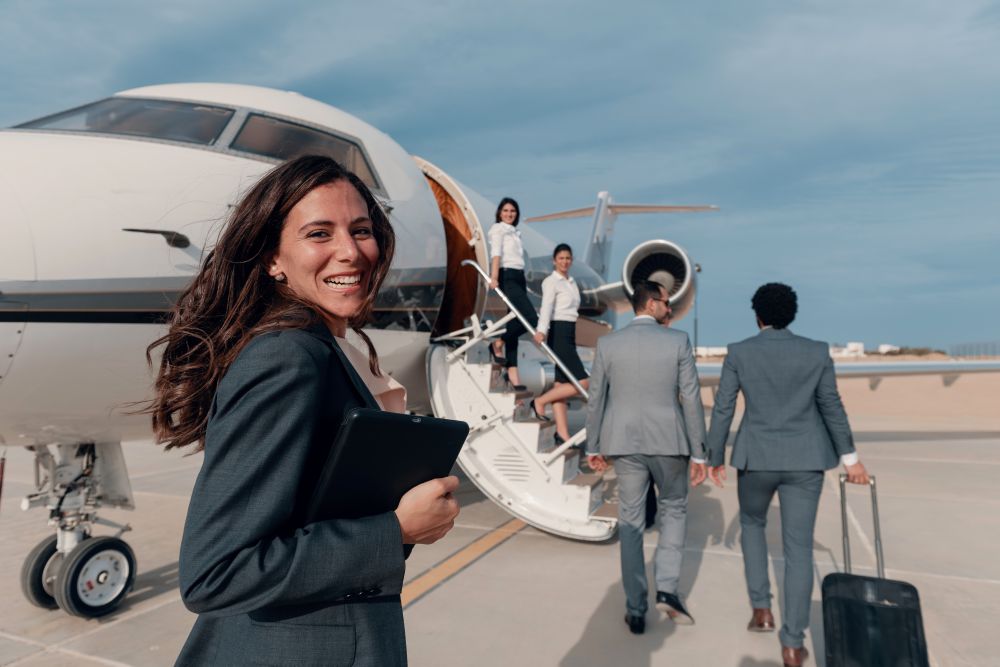 Business professionals boarding a private jet, with a woman smiling and holding a tablet while approaching the aircraft.