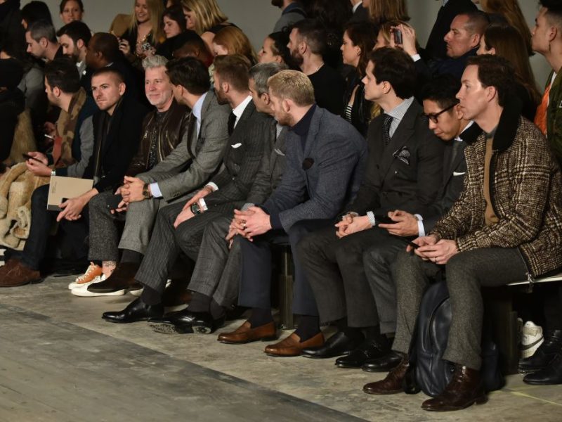 Men in stylish outfits seated in the front row at a fashion show, showcasing the latest trends in luxury style for Fall 2026.
