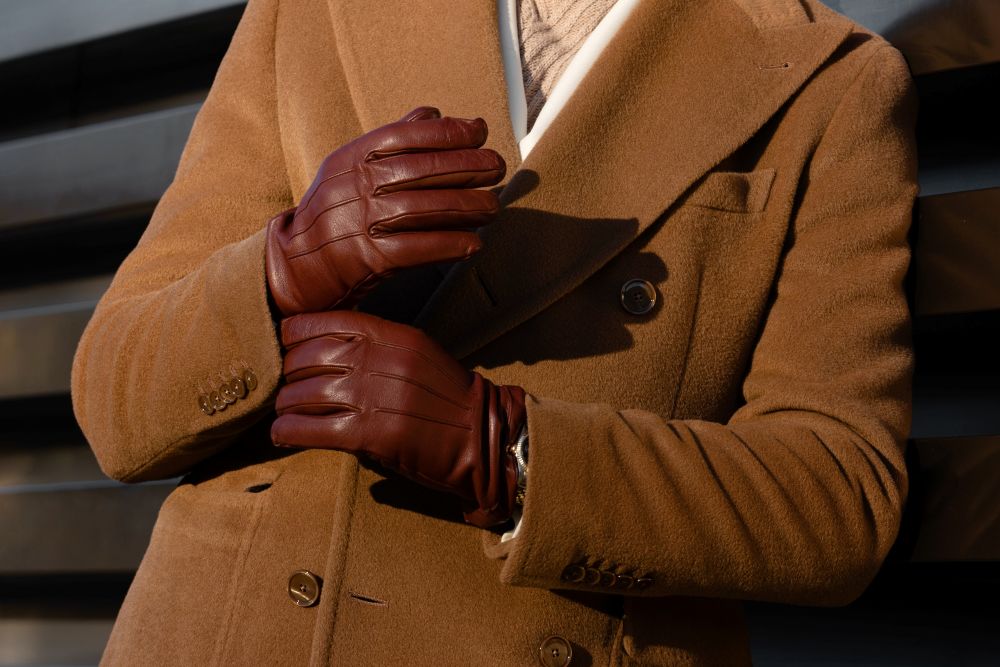 A man in a brown double-breasted coat wears stylish brown leather gloves, showcasing a luxury winter fashion look.