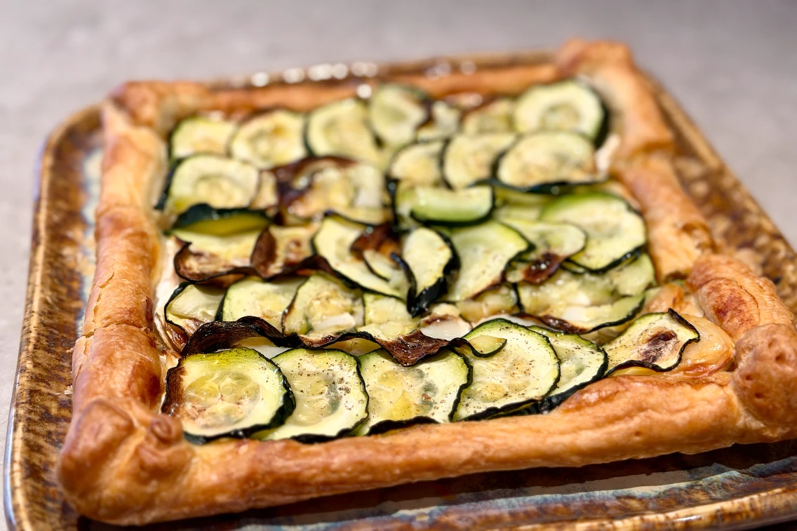 Vegetable tart topped with thinly sliced zucchini on a golden, flaky pastry crust.