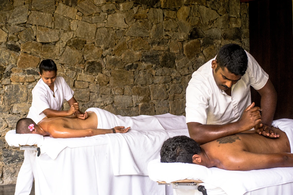 Couples enjoying massages at Santani Wellness Retreat with stone wall backdrop, emphasizing relaxation and healing.