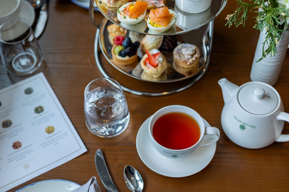 A tea cup with brewed tea sits next to a glass of water and an assortment of pastries on a table, with a menu visible.