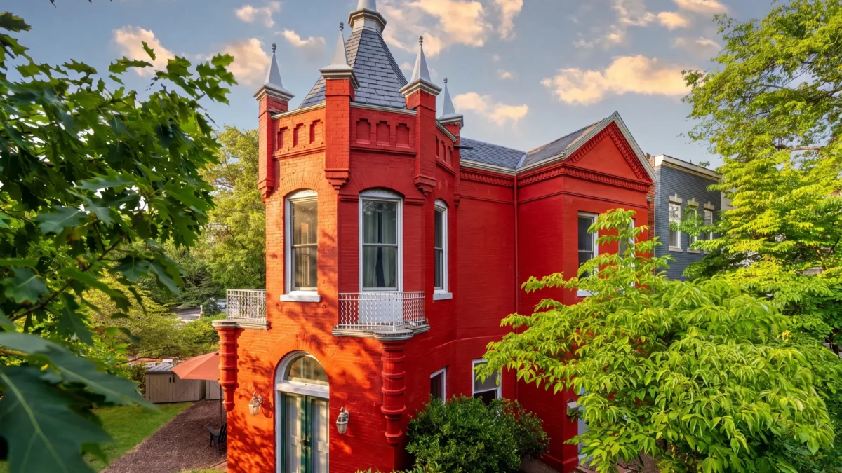 Victorian-style home with castle-like features surrounded by greenery in Capitol Hill, showcasing vibrant red brick and spires.