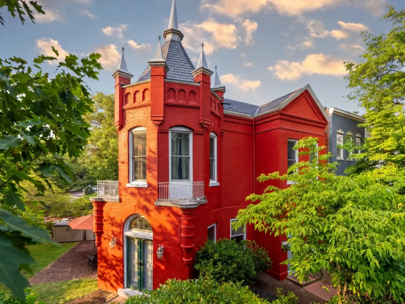 Victorian-style home with castle-like features surrounded by greenery in Capitol Hill, showcasing vibrant red brick and spires.