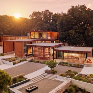Modern architectural retreat in Carmel set against a sunset, showcasing landscaped gardens and elegant structures.