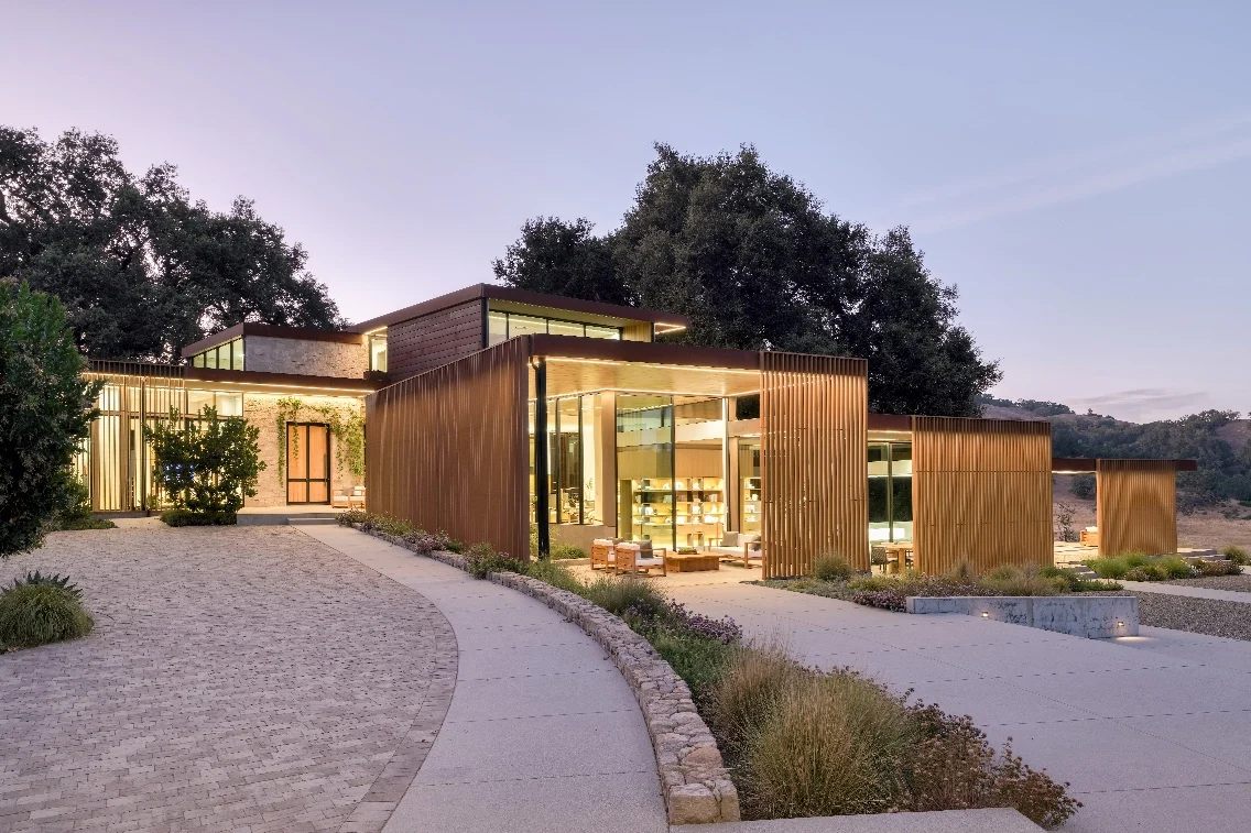 Modern architecture of the Meadow House in Carmel, featuring wooden panels and large glass windows amidst landscaped grounds.