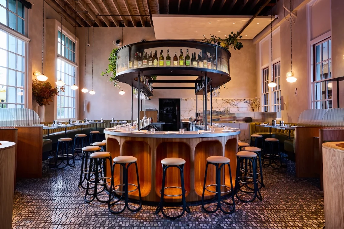 Modern bar with an elegant circular design, surrounded by wooden stools, in a stylish, brightly lit dining area.