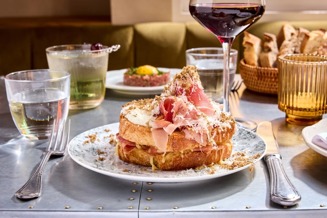 A beautifully plated croque monsieur with layers of ham and cheese, surrounded by glasses of water and wine on a dining table.