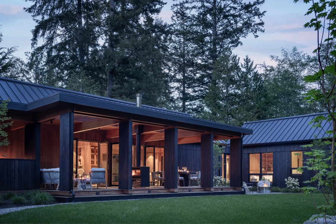 Modern luxury prefab home surrounded by trees, showcasing a wooden facade and inviting outdoor seating areas.