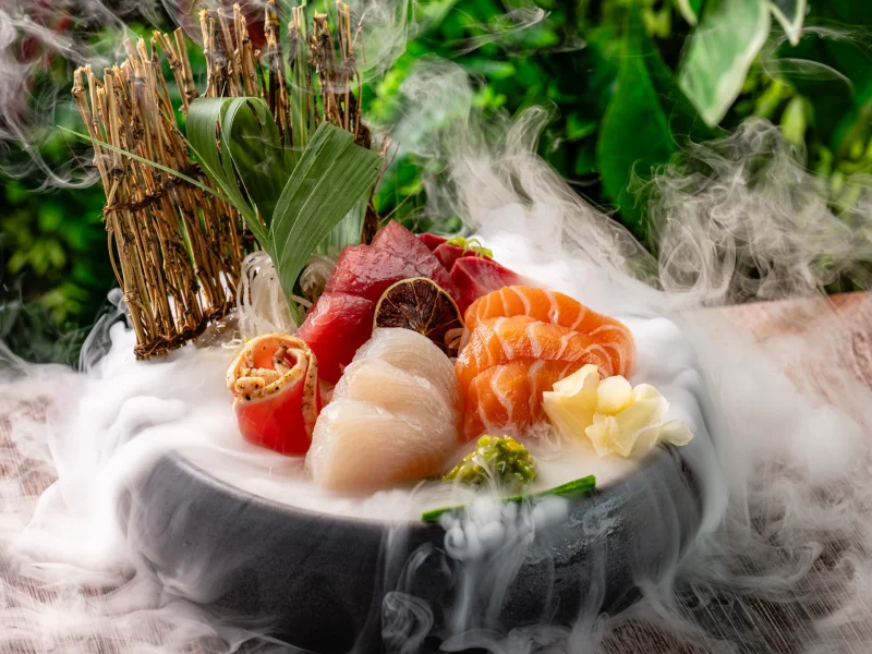 Sashimi platter presented with vibrant seafood and garnishes, surrounded by wisps of smoke on a rustic wooden table.