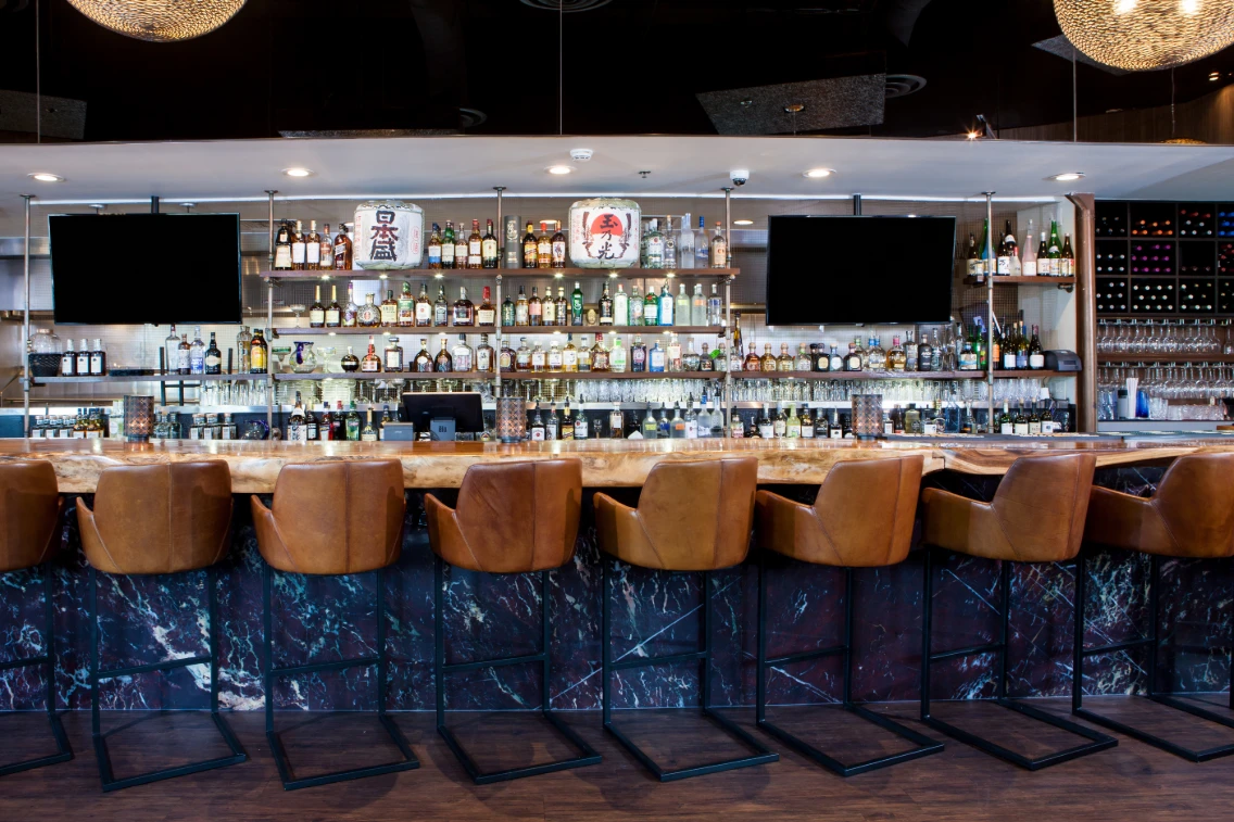 Stylish bar area featuring leather stools and a backdrop of various liquors displayed on shelves.