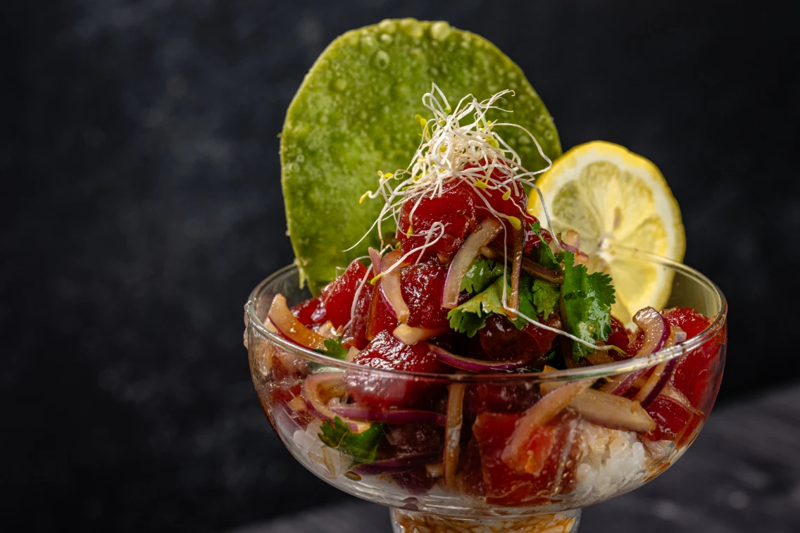 Ahi poke bowl topped with cilantro, sprouts, and a lime wedge, served in a glass dish for a vibrant culinary experience.
