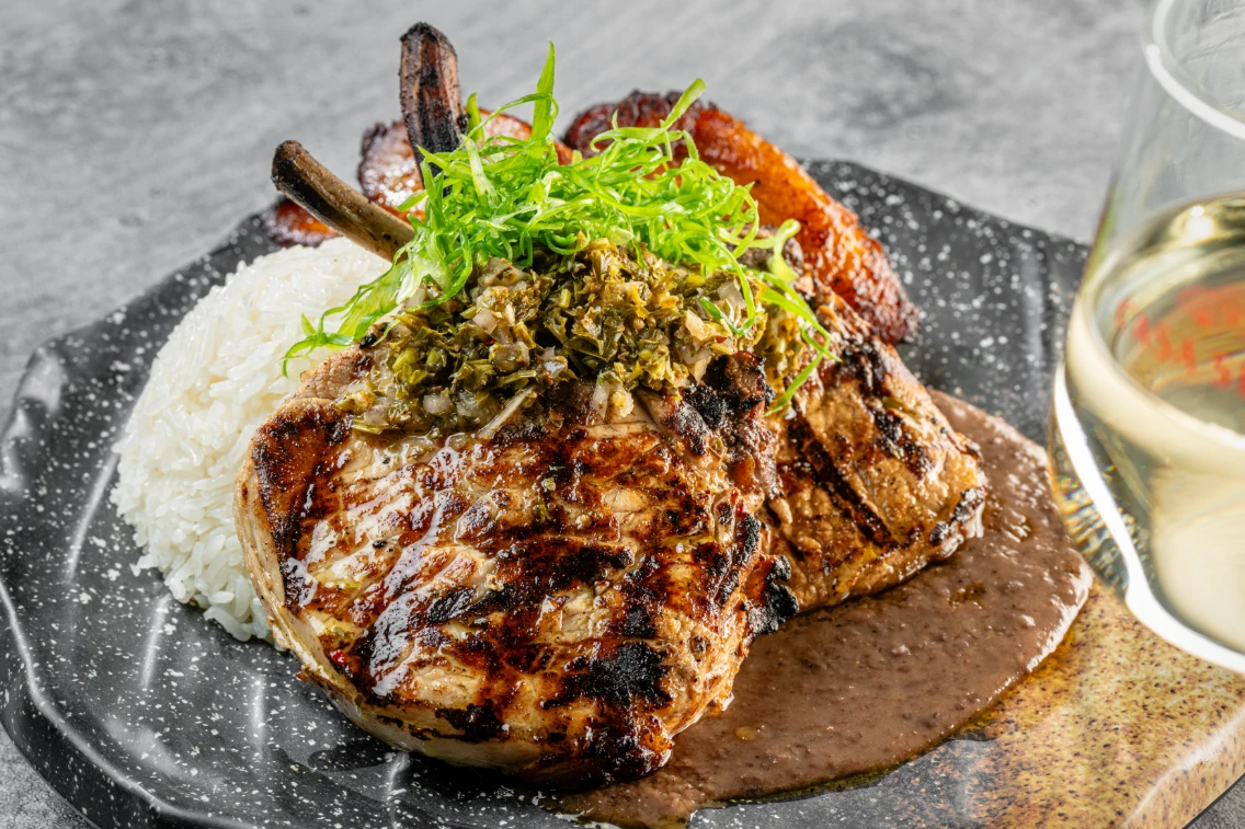 Mojo-marinated lechon served with rice, garnished with green onions and a flavorful sauce, accompanied by a glass of white wine.