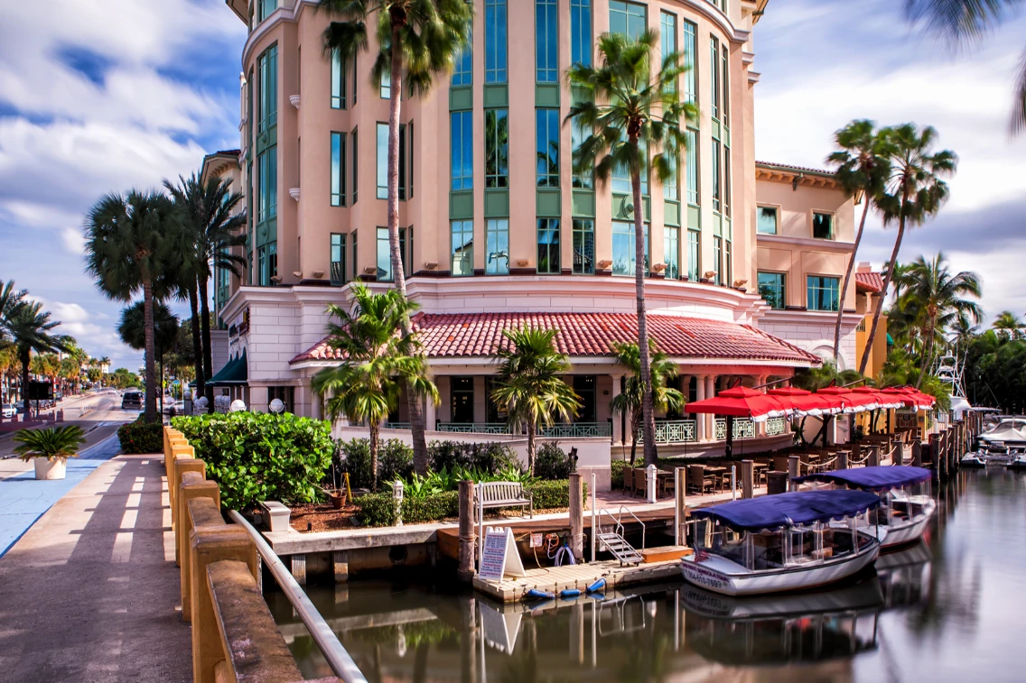 Casa Sensei on the Las Olas waterfront, featuring outdoor seating, palm trees, and boats docked along the canal.