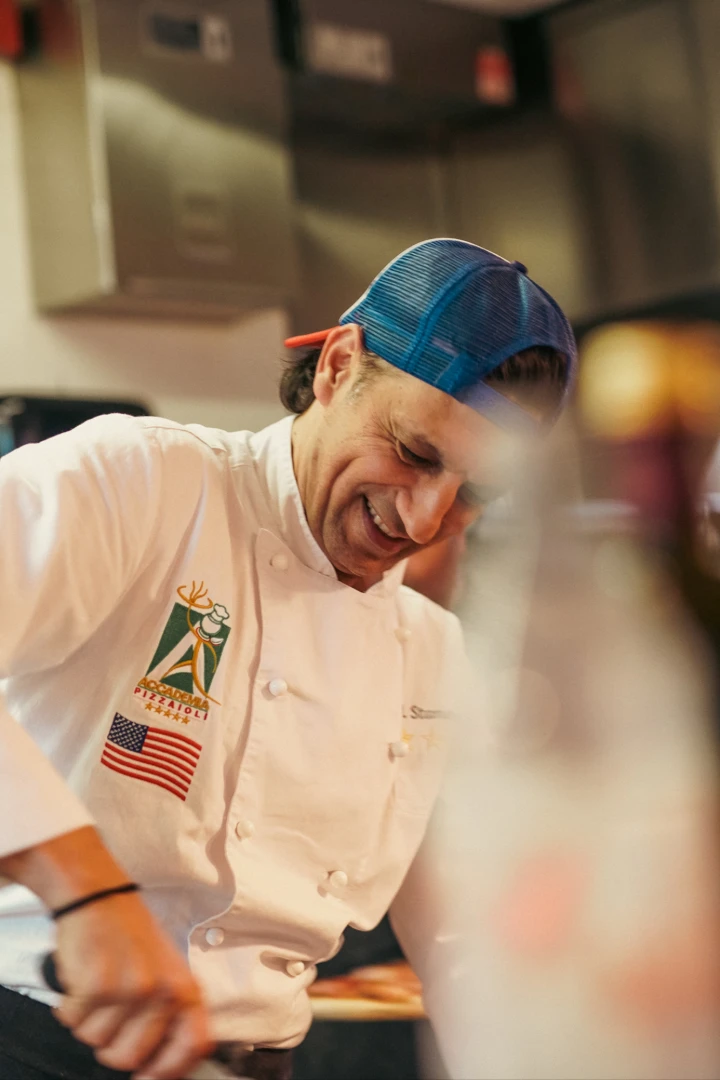 Chef smiling while preparing food in a modern kitchen, showcasing the blend of Italian heritage and contemporary culinary techniques.