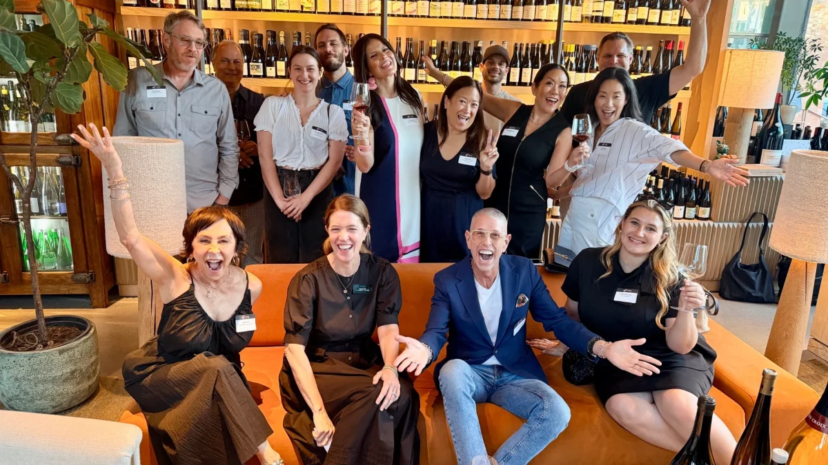 A joyful group of people gathered at a wine event, celebrating local cuisine while holding glasses and smiling.